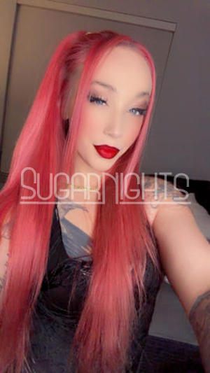 Miss Red, Denver escort with long red hair, blue eyes, red lipstick, and tattoos